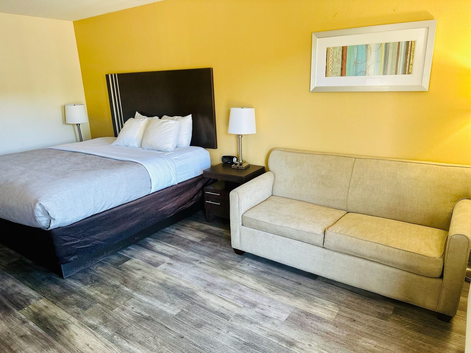 A hotel room with a bed, bedside tables, a sofa, and a framed picture on the wall.