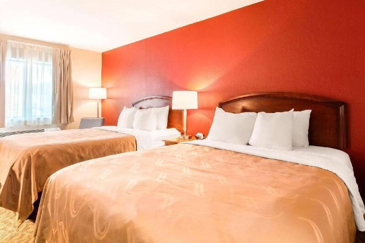 A hotel room with two beds, a window with curtains, and a lamp on each side of the bed.