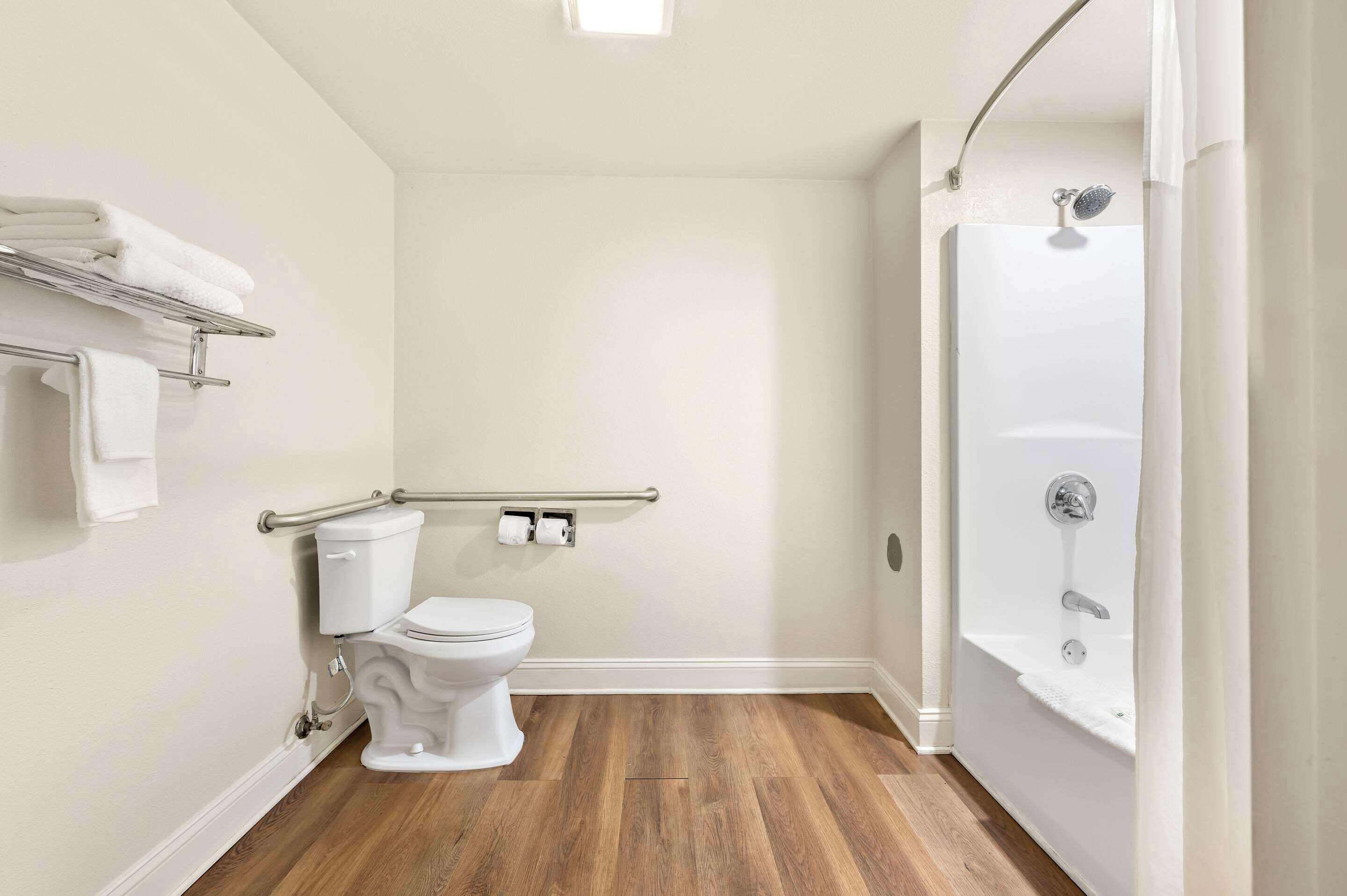 A bathroom with a toilet, a shower, and a wooden floor.