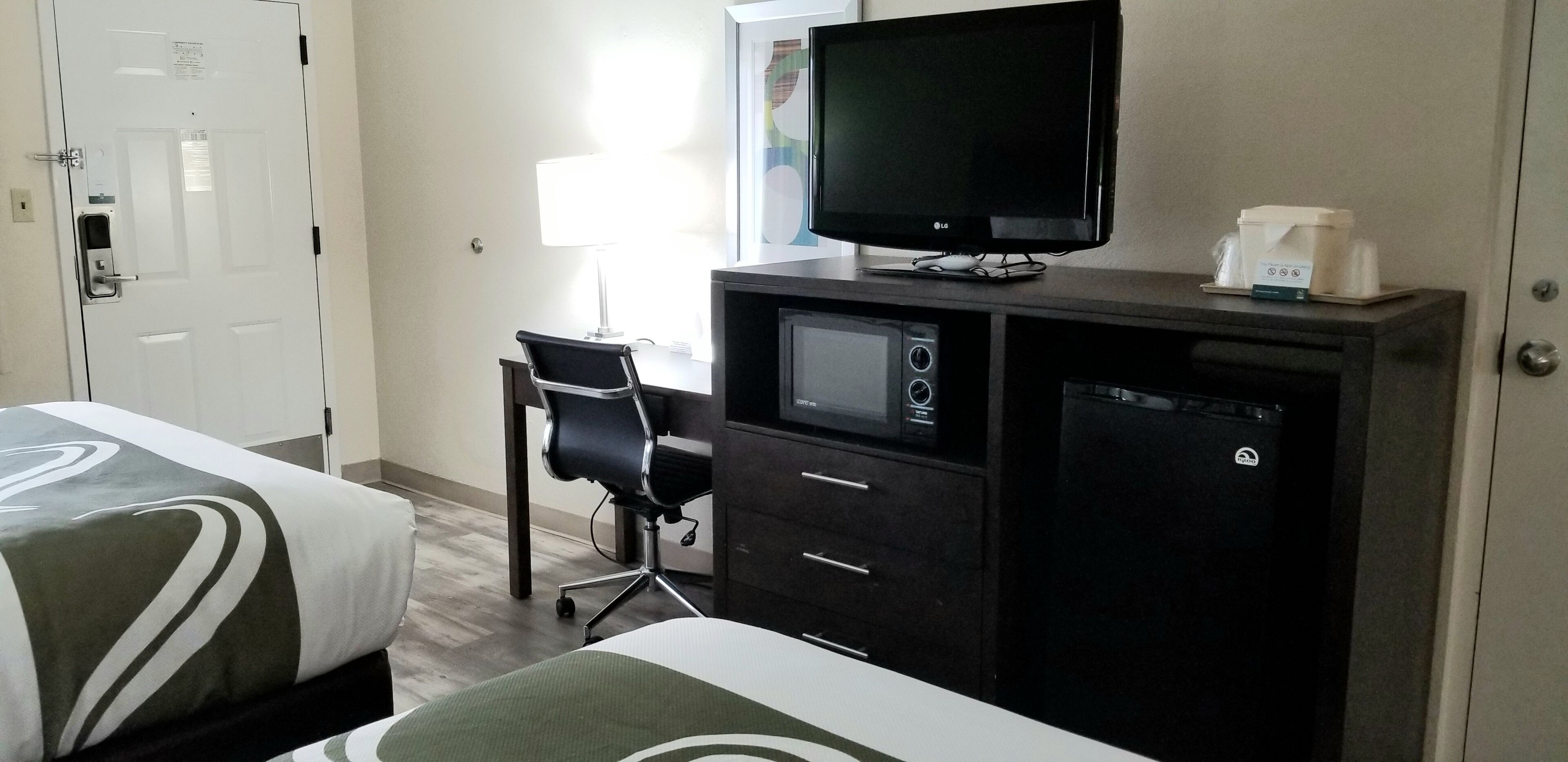 Une chambre d’hôtel équipée d’un lit, d’un bureau avec une chaise, d’une télévision, d’un four à micro-ondes et d’une machine à café.