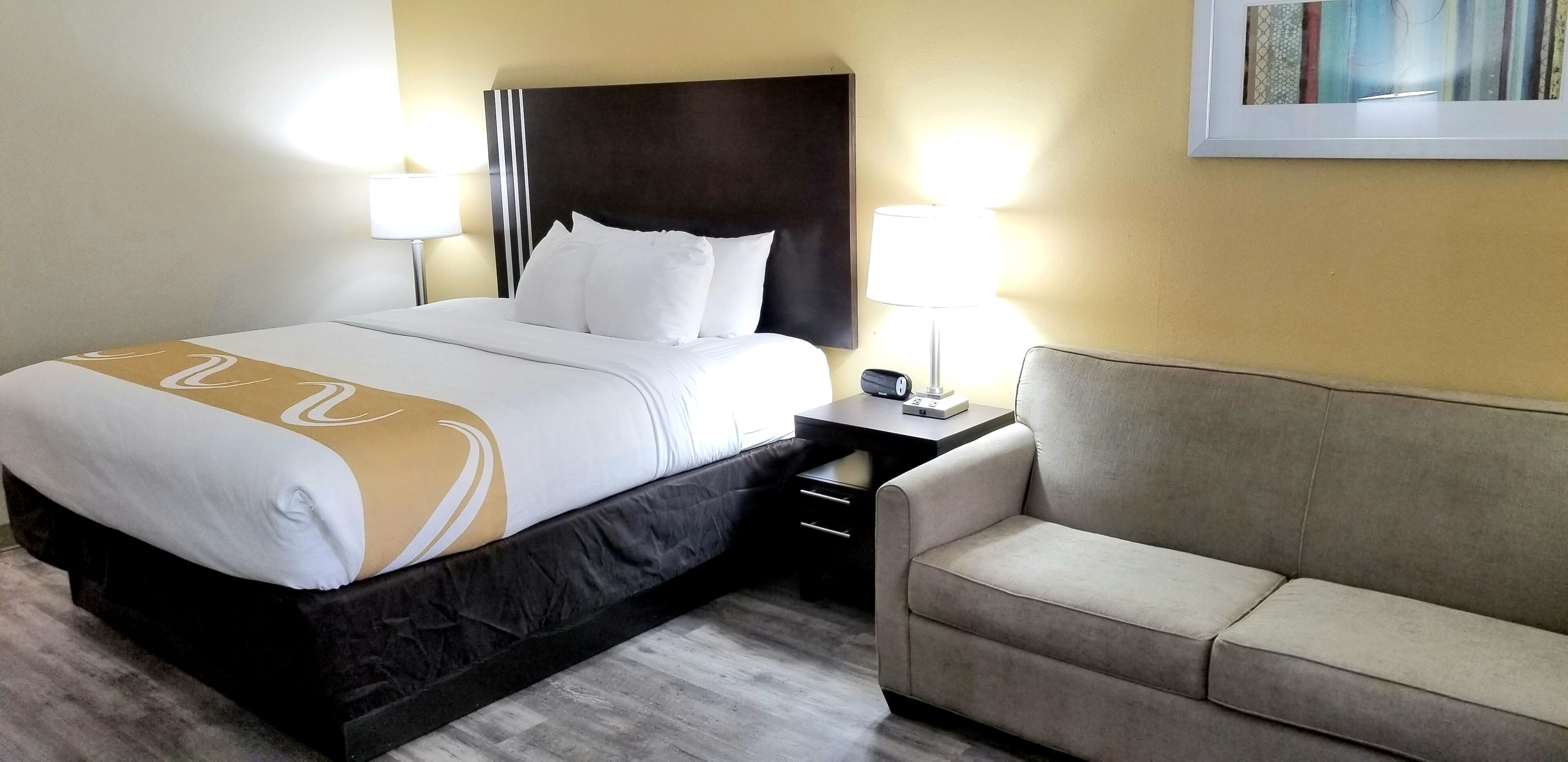 A hotel room with a bed, bedside tables, a lamp, and a sofa.
