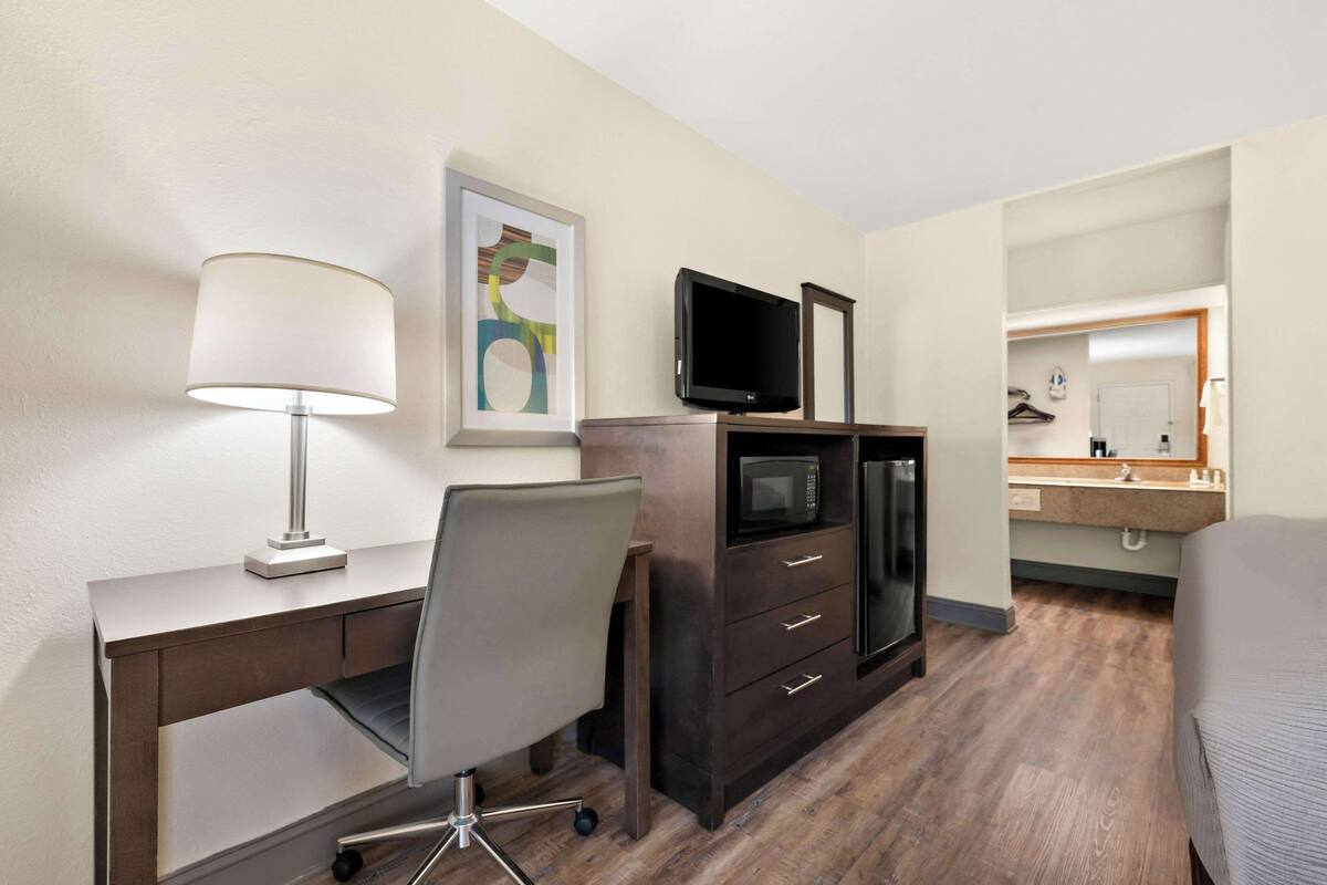 A hotel room with a desk, chair, TV, microwave, and a bed.