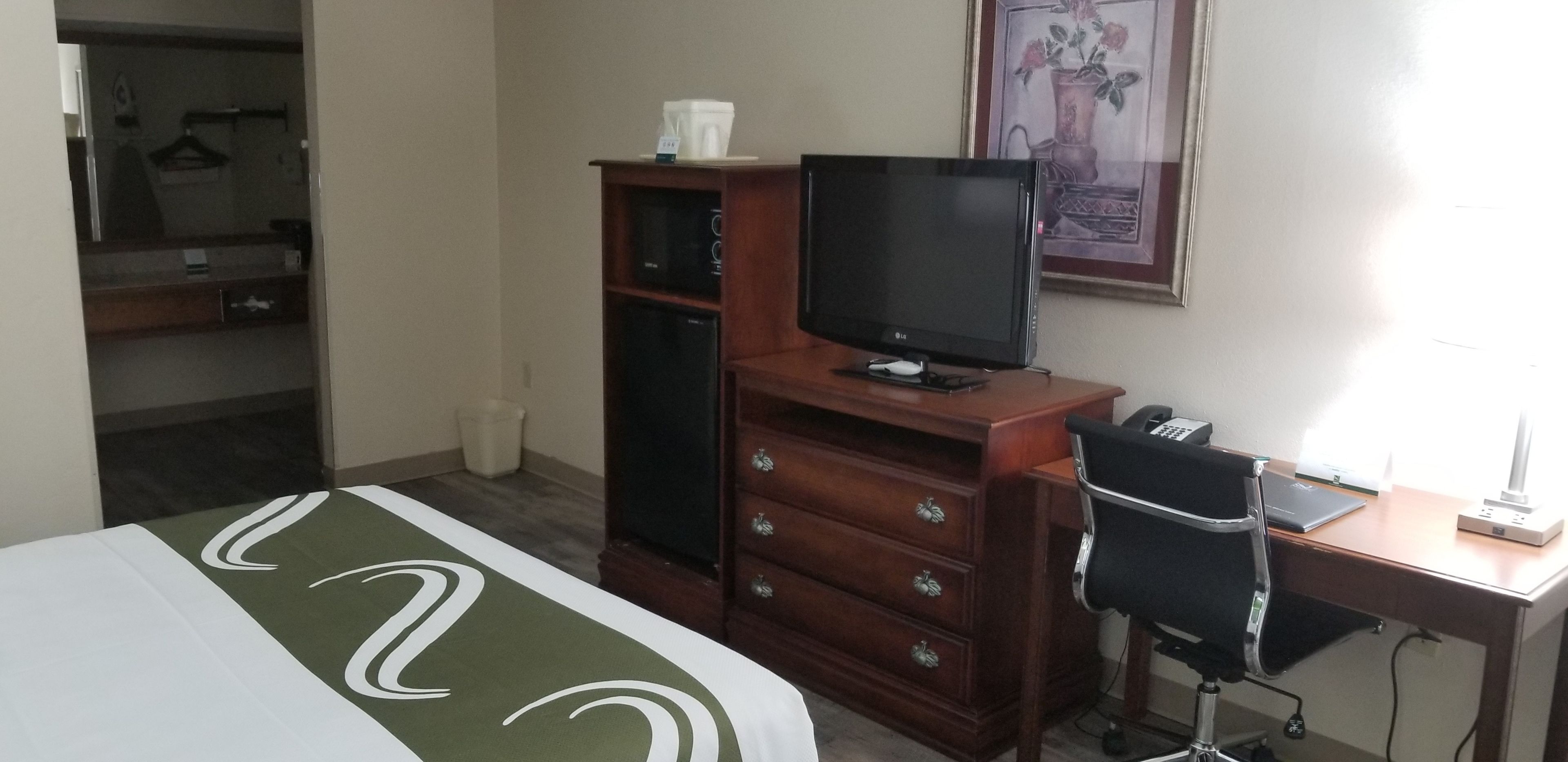 Une chambre d’hôtel avec un lit, un bureau avec un ordinateur, une télévision, une armoire et une salle de bain visible au fond.
