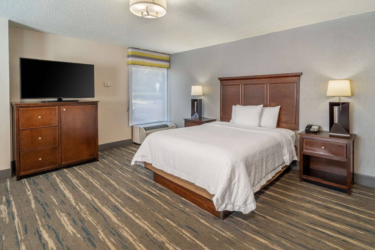 Une chambre d’hôtel avec un grand lit, une télévision, un bureau avec une lampe et une fenêtre donnant sur un beau paysage.