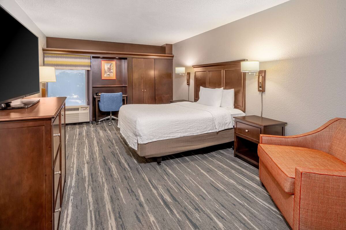 Une chambre d’hôtel avec un grand lit, un bureau avec un ordinateur, une chaise, une télévision et un canapé.