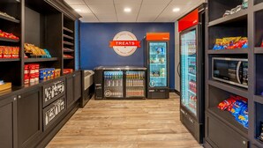 Una tienda con estantes llenos de aperitivos y bebidas, una sección refrigerada y un letrero que indica que ofrece productos de conveniencia.