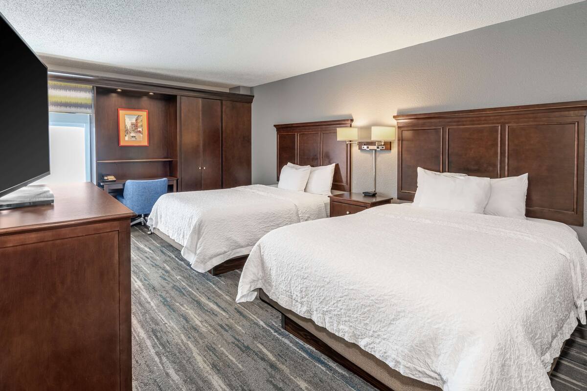Une chambre d’hôtel avec deux lits, un bureau, une chaise et un téléviseur.