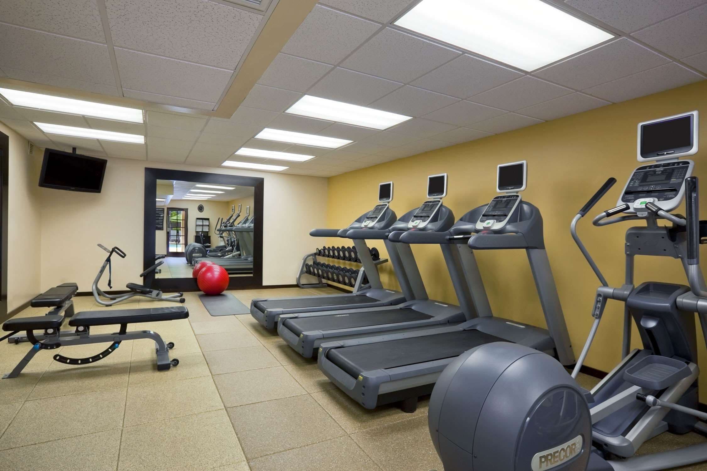 Une salle de sport équipée de tapis de course, d’un banc, d’haltères et d’un ballon d’exercice rouge.