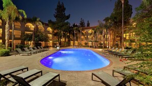 A swimming pool surrounded by lounge chairs and palm trees, with a building in the background.