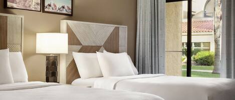 A hotel room with two beds, a nightstand, a lamp, and a large window with a view of the outdoors.
