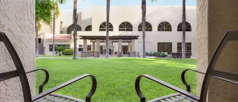 A courtyard with a lawn, palm trees, and a building with arched windows.