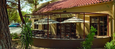 A building with a red-tiled roof and a covered patio area with tables and umbrellas.