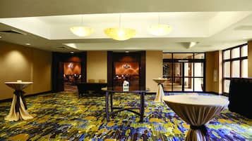 A hotel lobby with a colorful carpet, round tables, and a seating area with chairs.