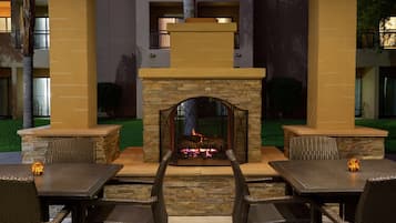 Un patio al aire libre con chimenea de piedra, mobiliario de mimbre y vistas al interior del edificio.