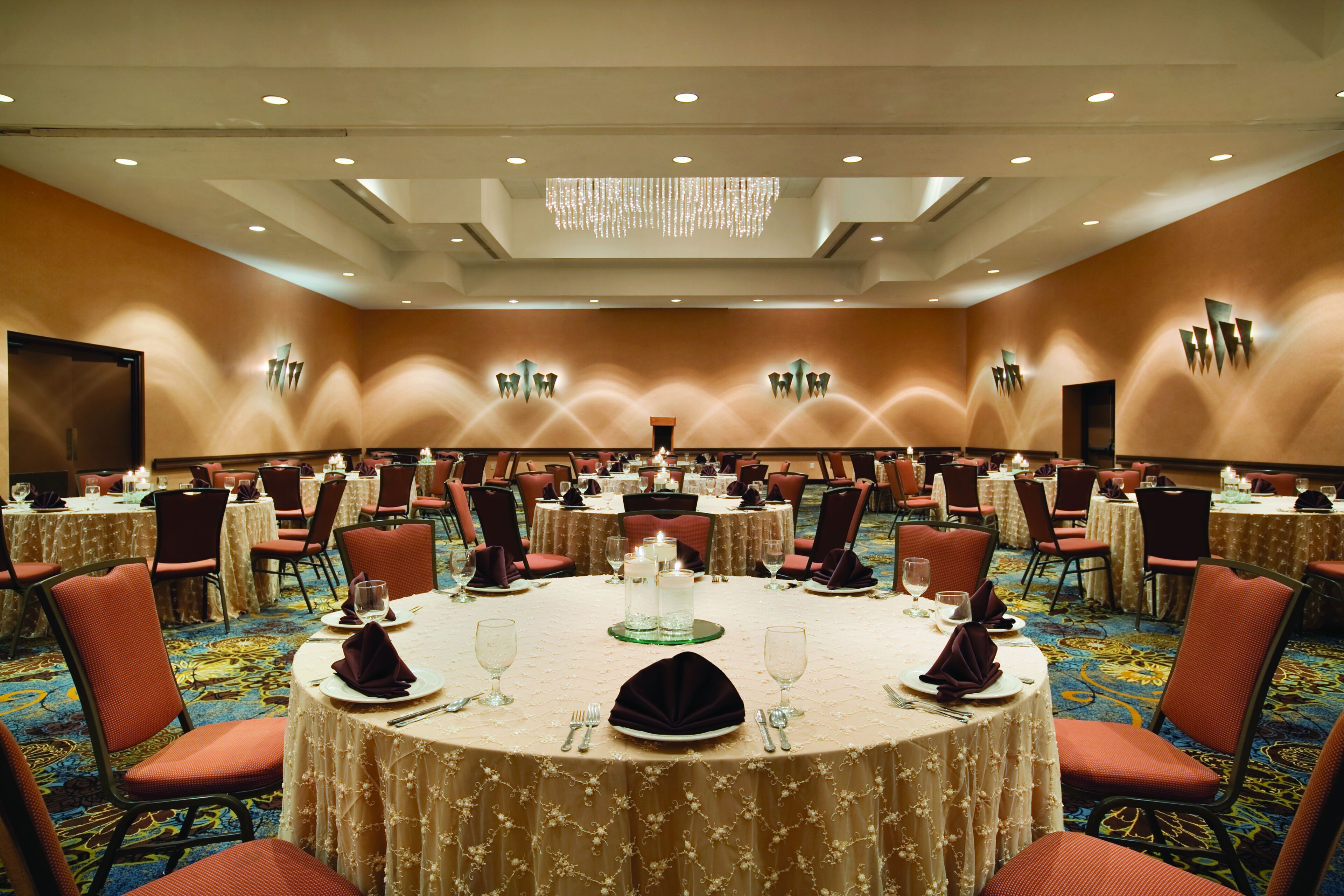 A large banquet hall with round tables, chairs, and a chandelier.