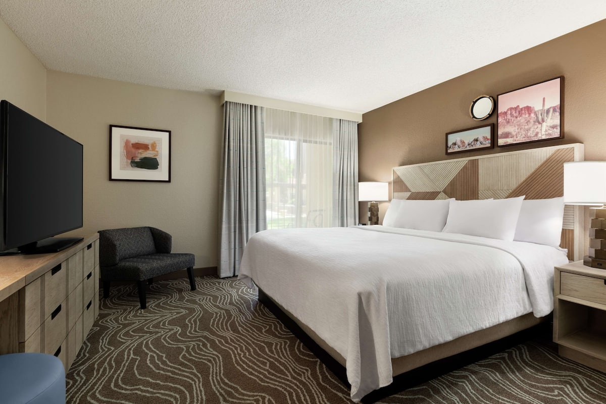 A hotel room with a large bed, a TV, a desk, and a chair.