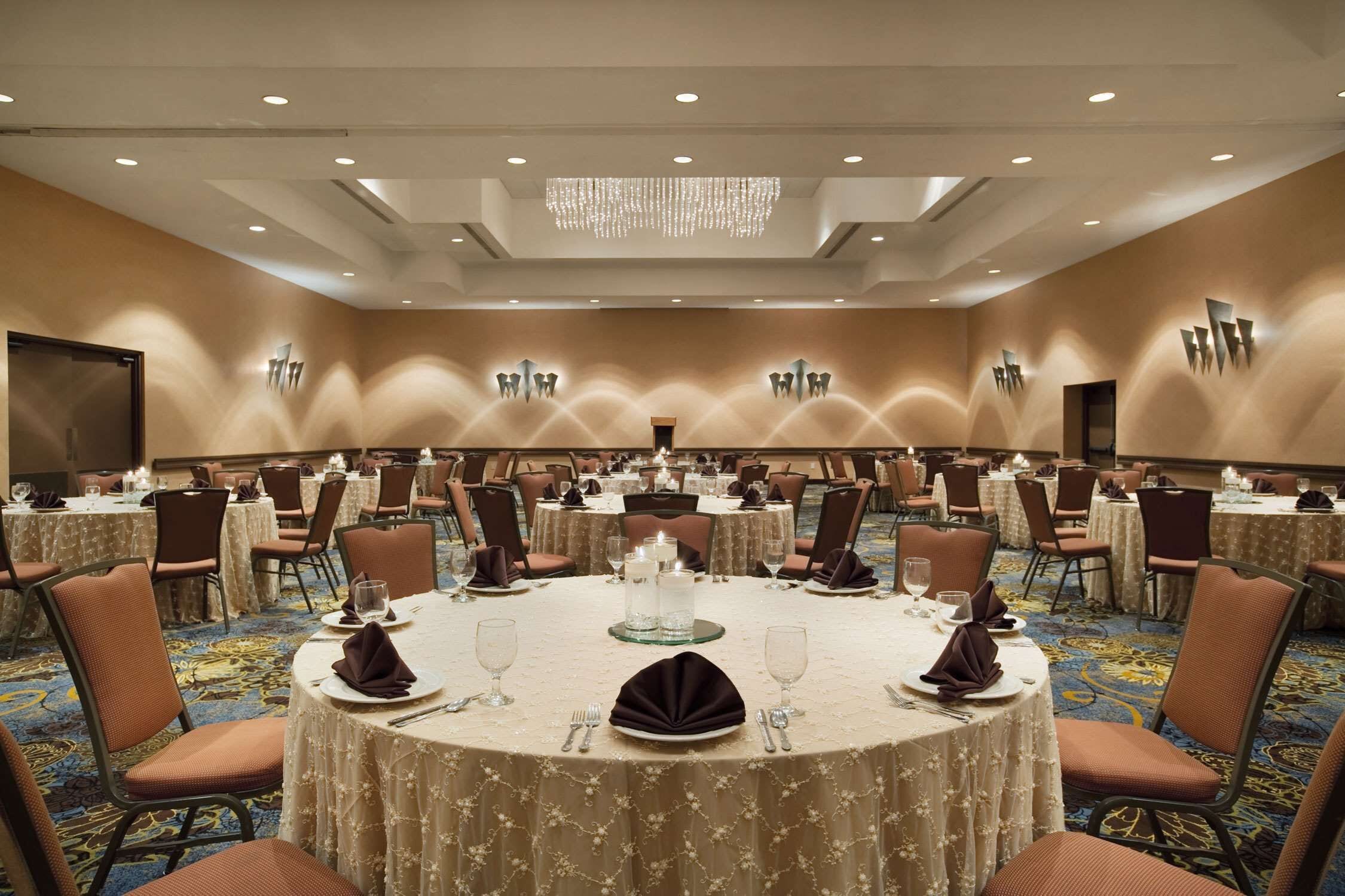 Une grande salle de conférence équipée de tables rondes, de chaises et d’un lustre.