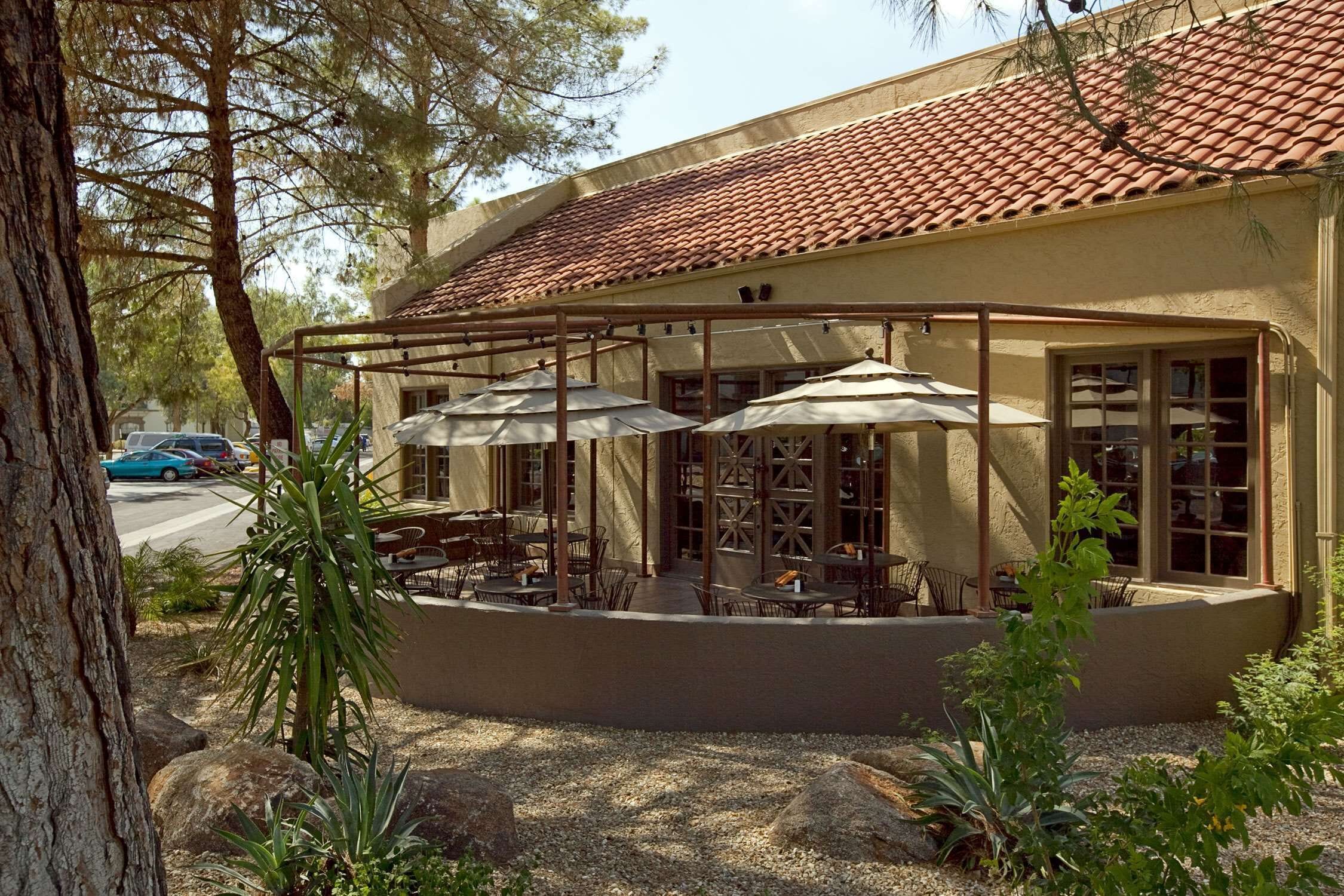 A building with a tiled roof, outdoor seating area with umbrellas, and a view of the street.