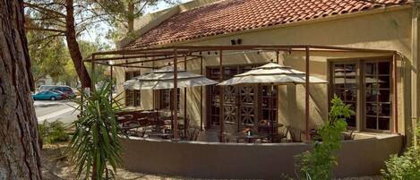 A building with a tiled roof, outdoor seating area with umbrellas, and a view of the street.