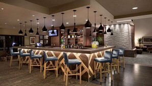 A bar area with multiple seating options, a television, and a variety of bottles and glasses on shelves.