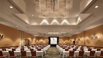 A conference room with rows of tables and chairs, a large screen at the front, and a chandelier.