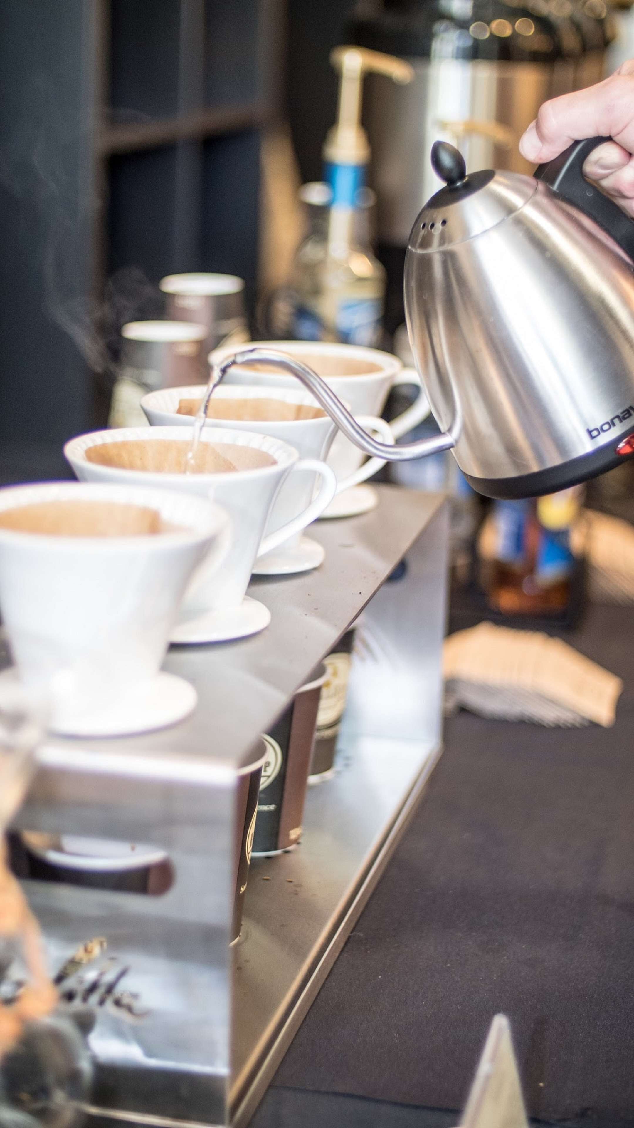 A coffee machine dispensing coffee into white cups on a stainless steel counter.