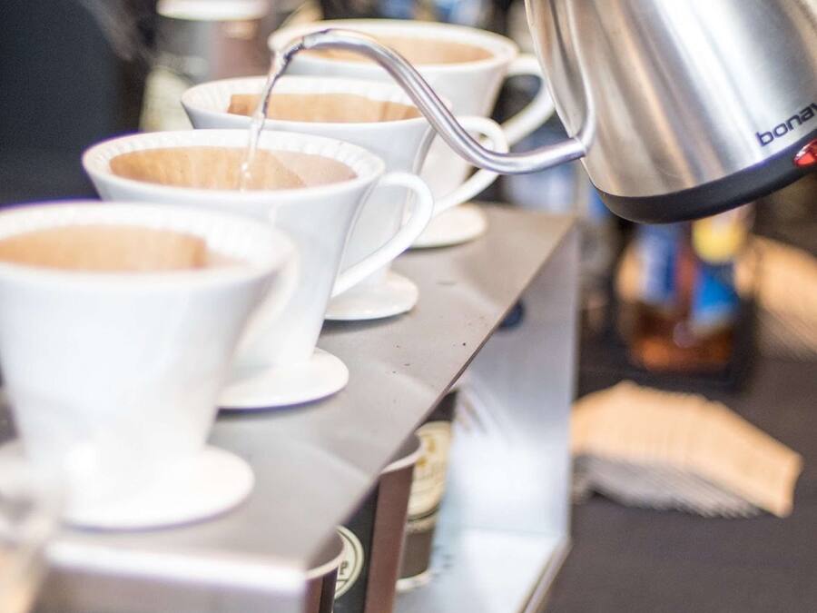 A coffee machine dispensing coffee into white cups on a stainless steel counter.