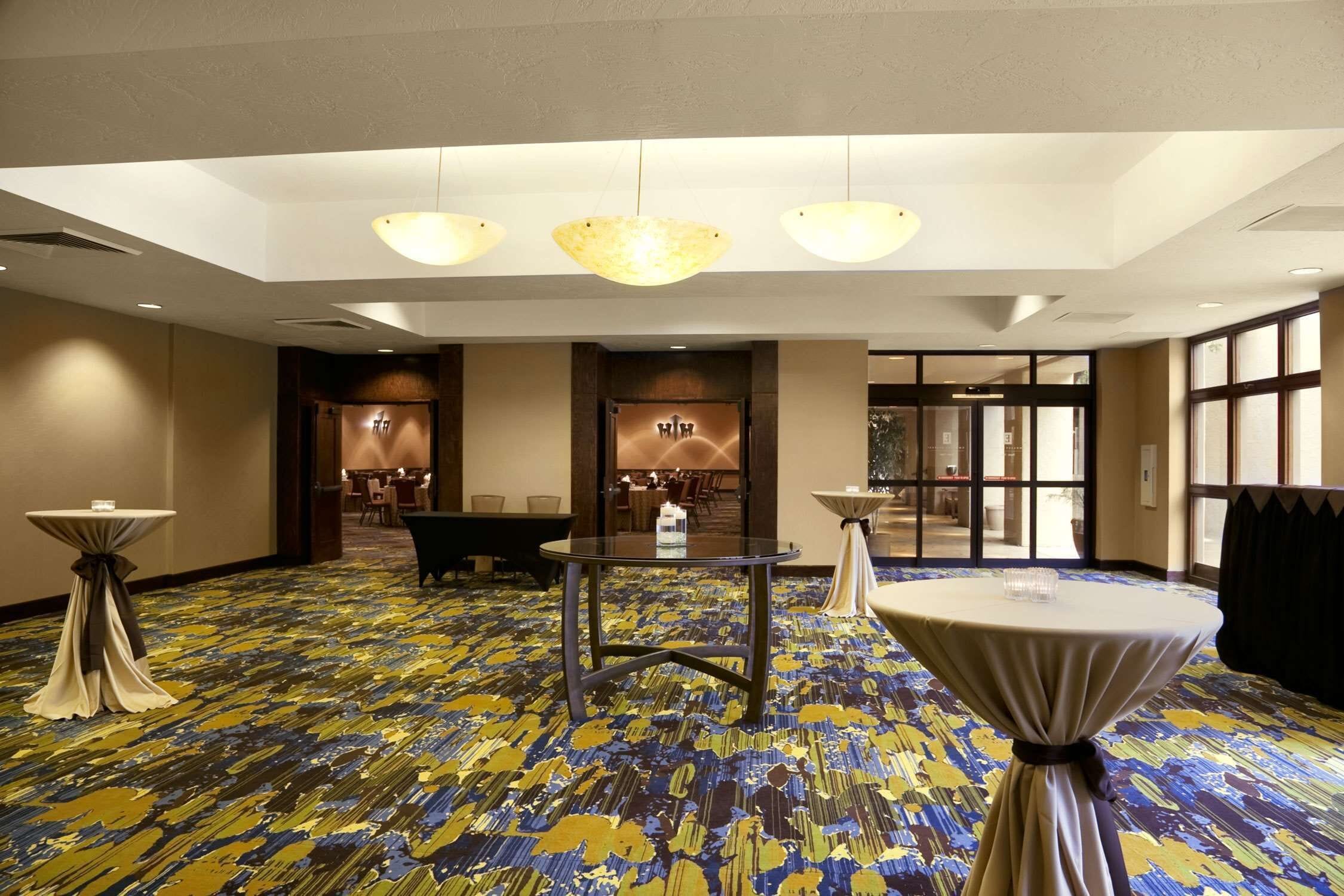 Un vestíbulo de hotel con alfombra estampada, mesas redondas y un candelabro.