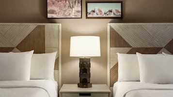 A hotel room with two beds, a nightstand with a lamp, and two framed pictures on the wall.
