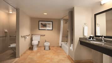 A modern bathroom with a toilet, bidet, bathtub, and a large mirror.
