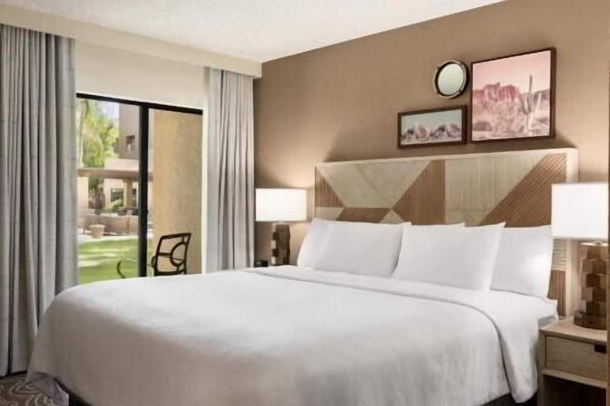 A hotel room with a large bed, two bedside tables, a window with curtains, and a view of the outdoors.