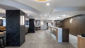 A modern hotel lobby with a reception desk, seating area, and a large marble column.