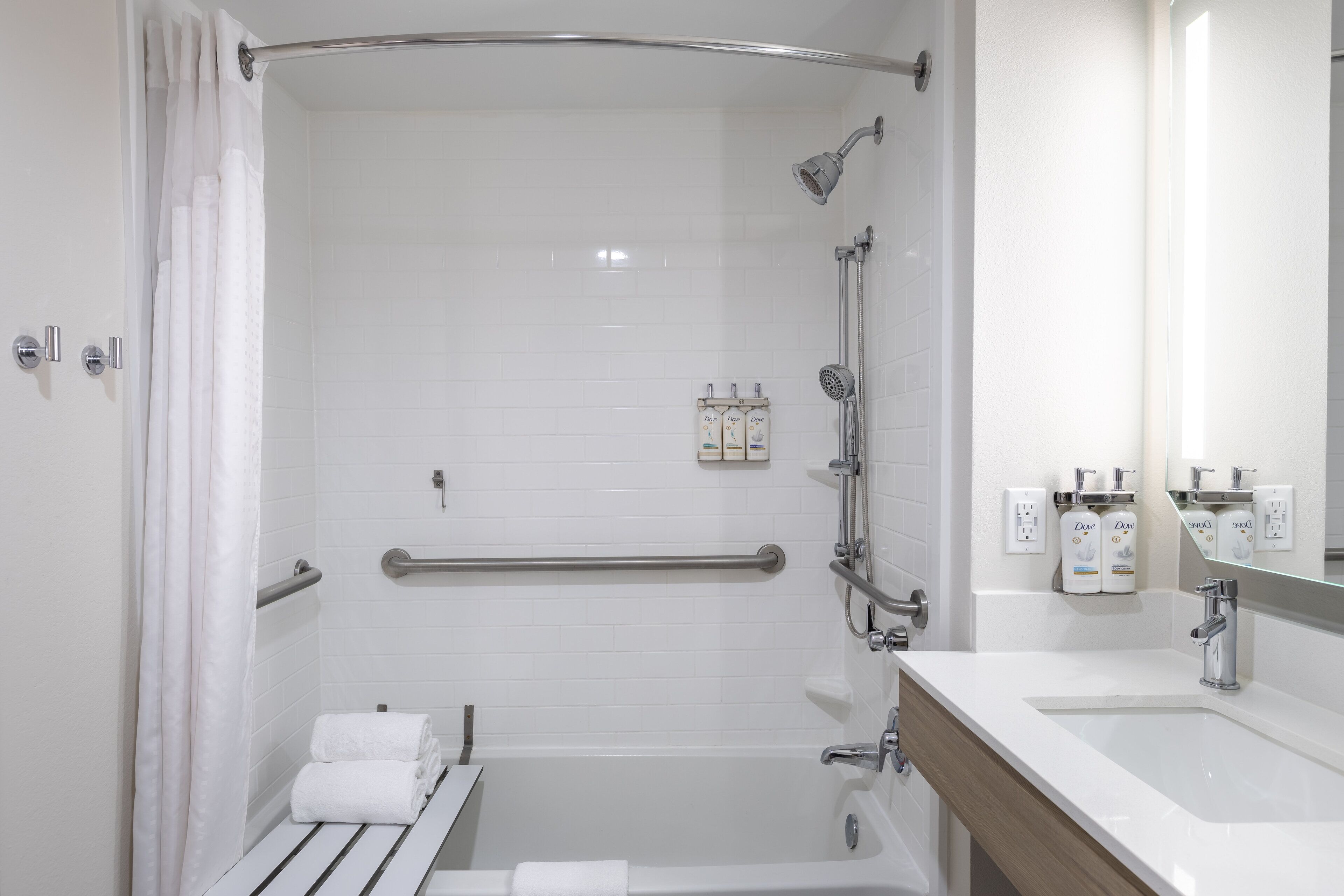 A modern bathroom with a shower, grab bars, a bathtub, and a sink with a mirror.