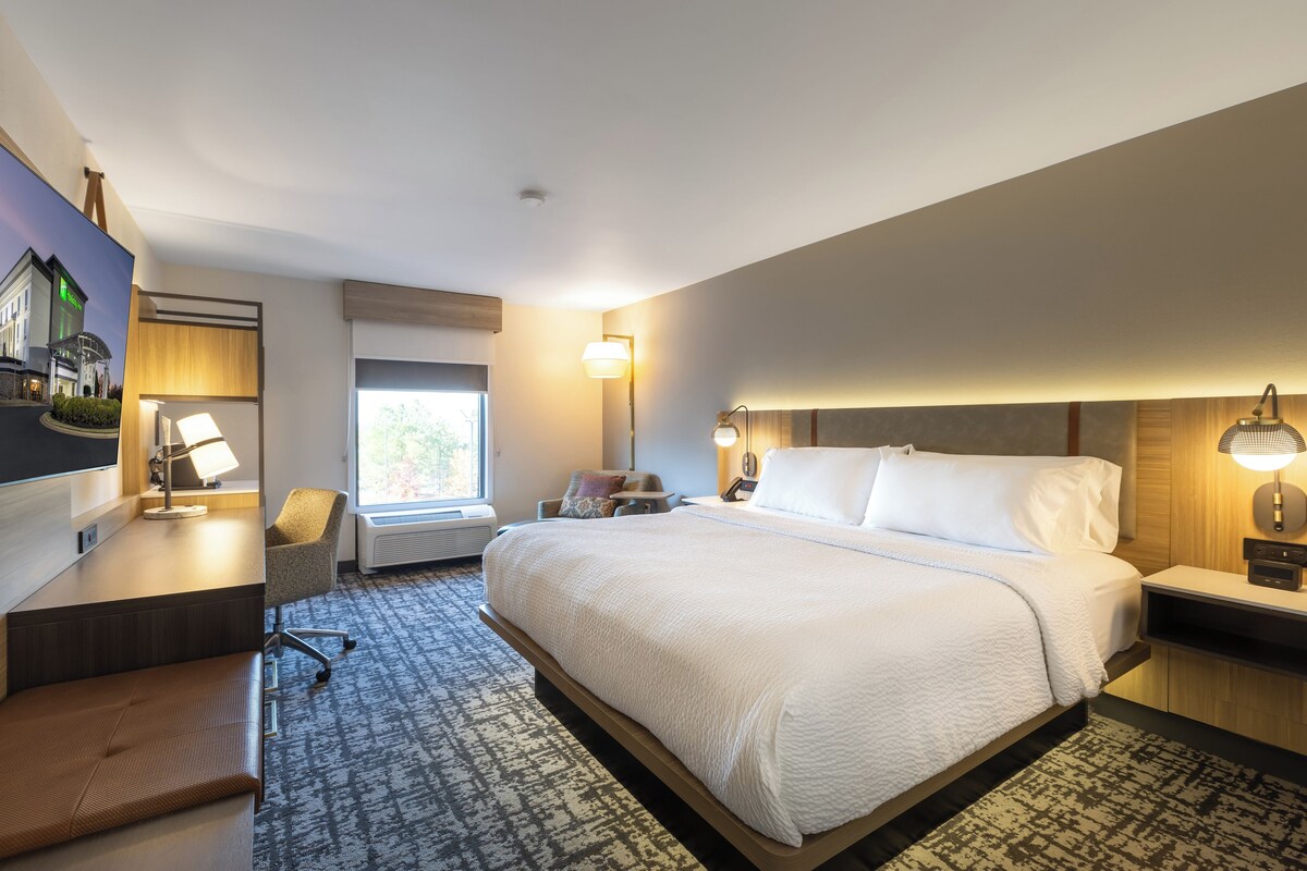 A hotel room with a large bed, a desk with a chair, a window, and a wall-mounted TV.