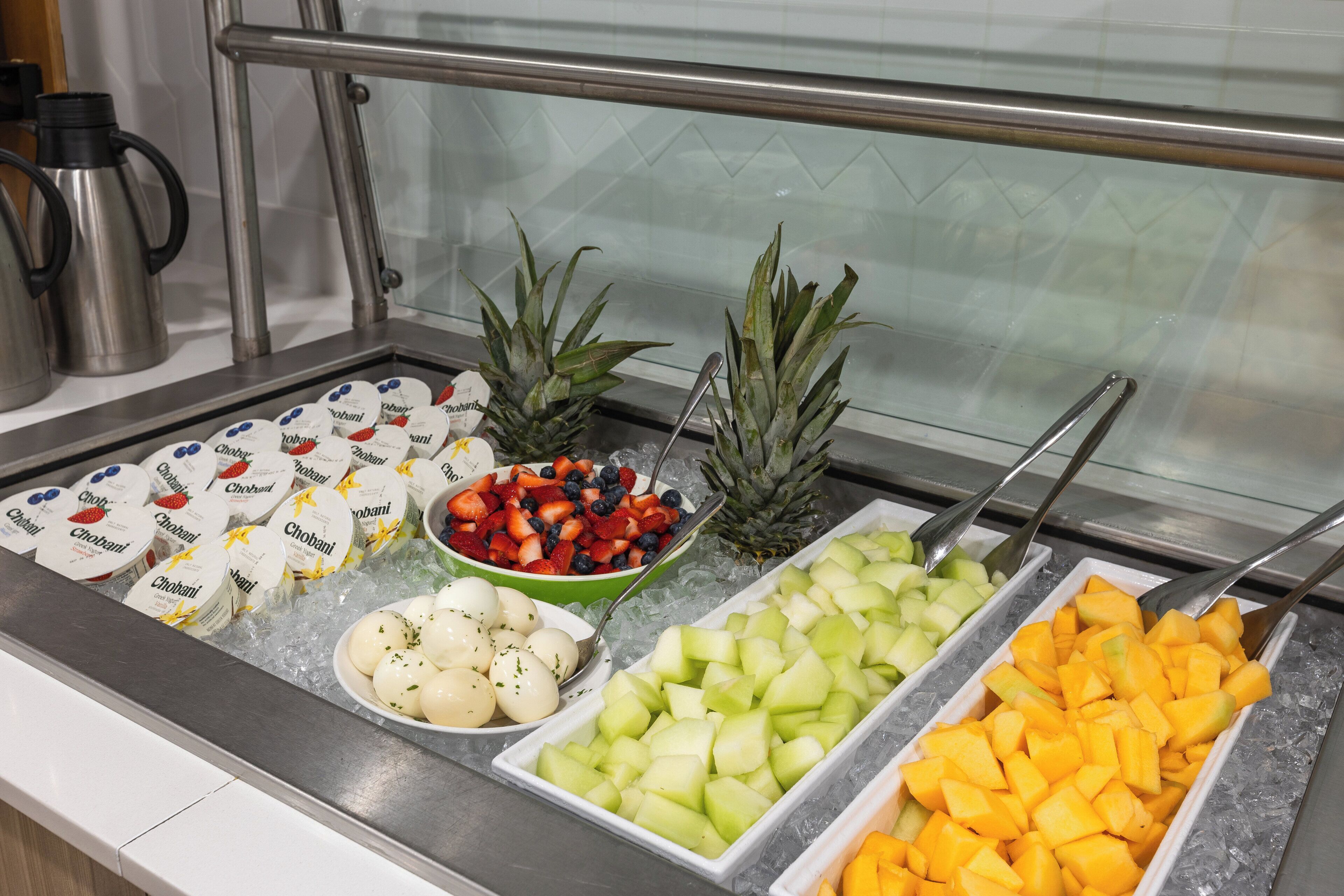 A buffet with various food items including yogurt, fruits, and a pineapple.