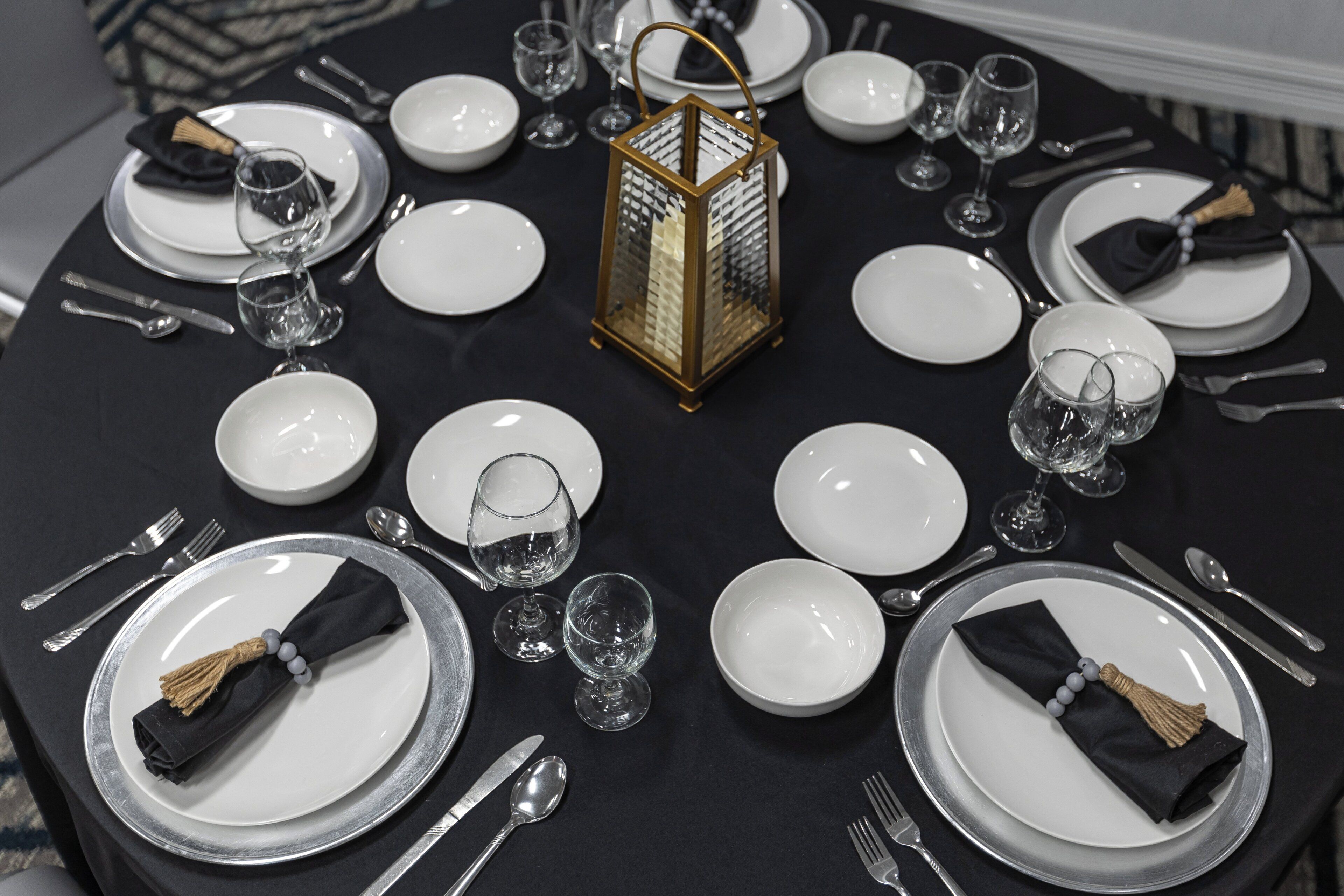 A round dining table set with plates, glasses, cutlery, and a central decorative lantern.