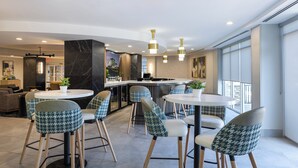Un intérieur moderne avec des tables rondes, des chaises à motifs pied-de-poule, un coin bar et une vue dégagée grâce à de grandes fenêtres.