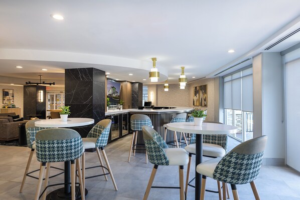 A modern interior with round tables, houndstooth patterned chairs, a bar area, and a view through large windows. - Holiday Inn Anderson by IHG (Anderson)