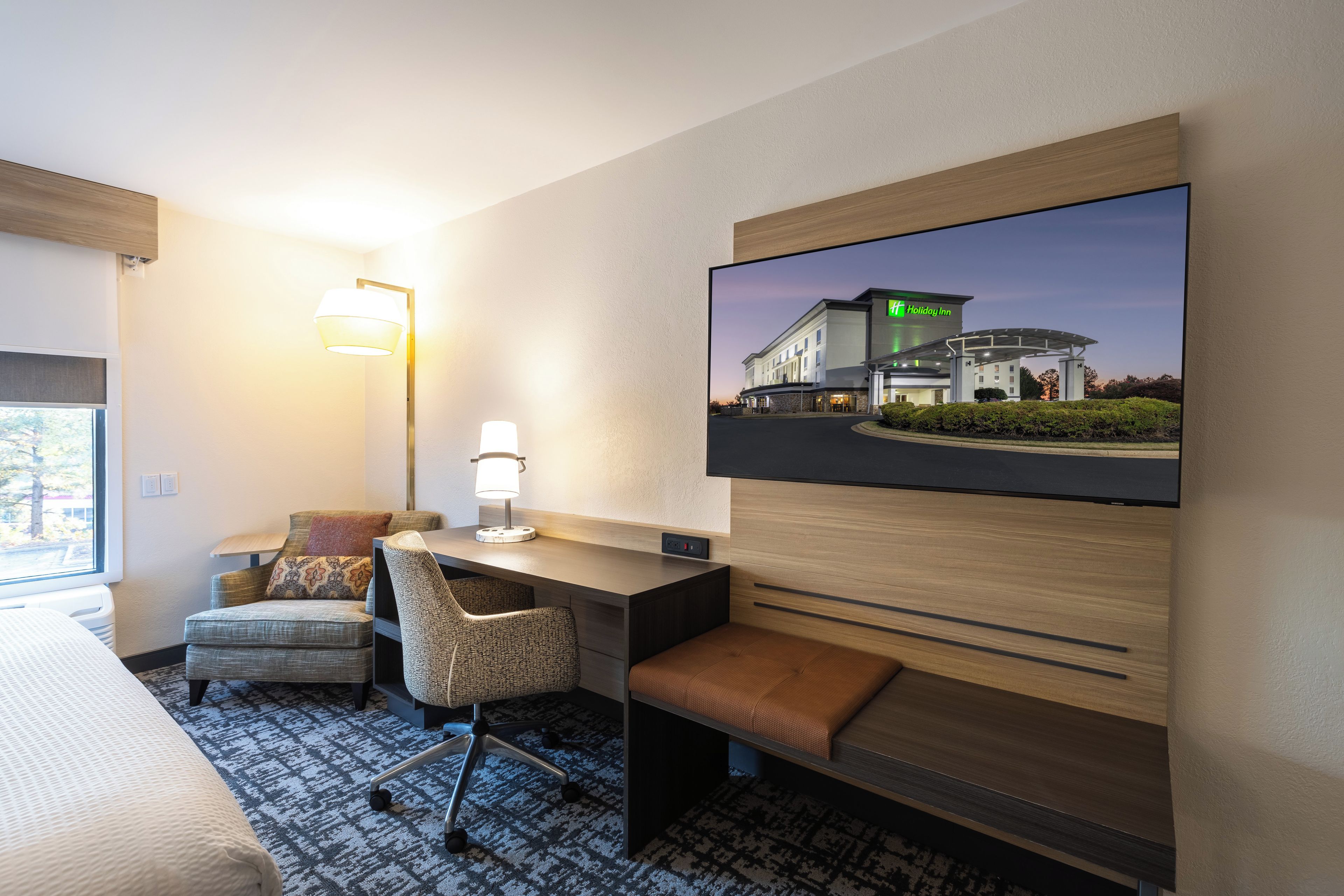 Une chambre d’hôtel comprenant un lit, un bureau avec une chaise, un téléviseur fixé au mur et une lampe.