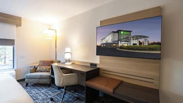Une chambre d’hôtel comprenant un lit, un bureau avec une chaise, un téléviseur fixé au mur et une lampe.