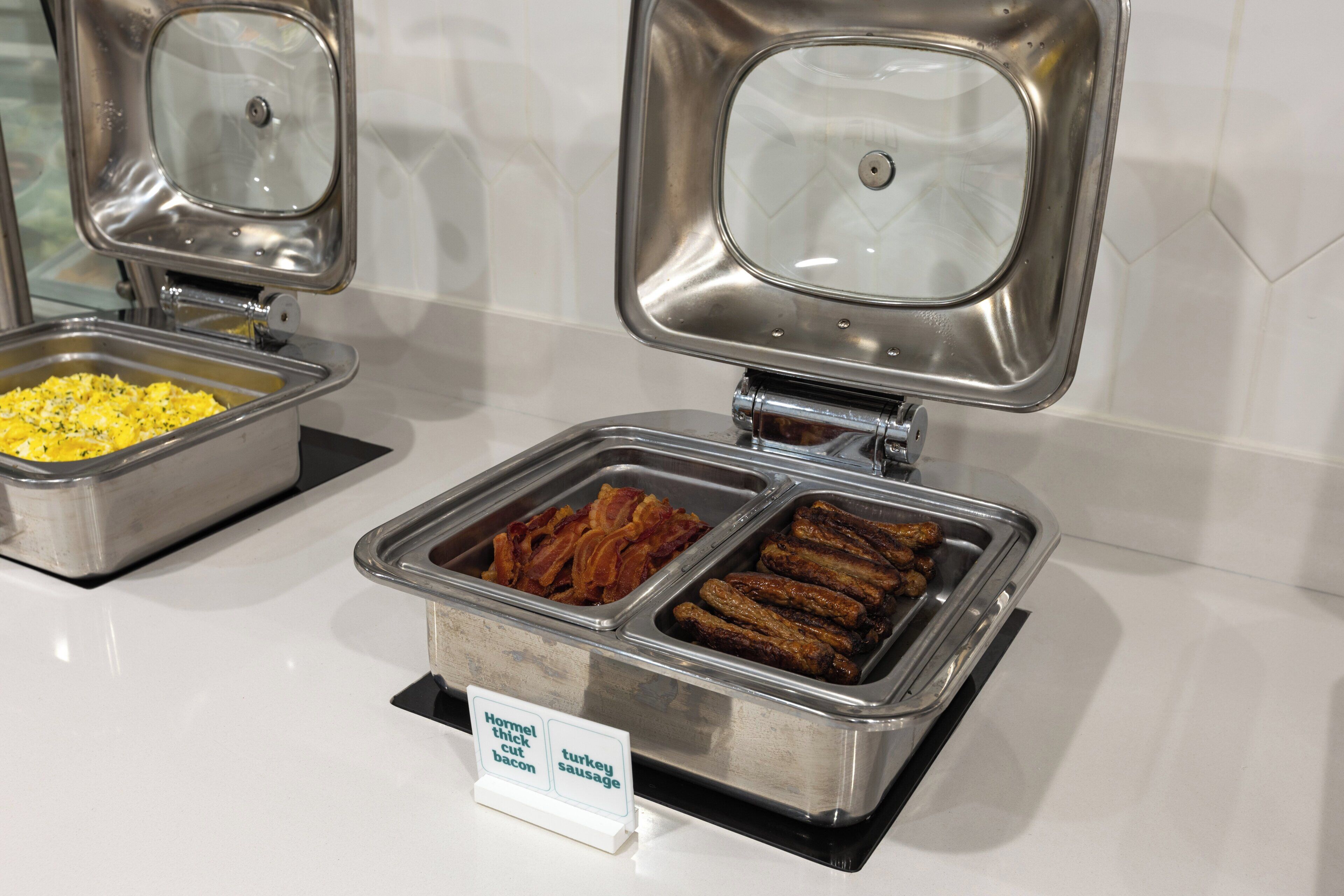 A buffet with labeled containers of food including bacon, turkey, and sausage.