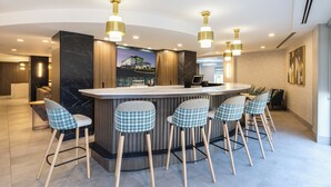 Un espace bar moderne avec un comptoir en marbre, des chaises à motifs pied-de-poule et des luminaires suspendus.