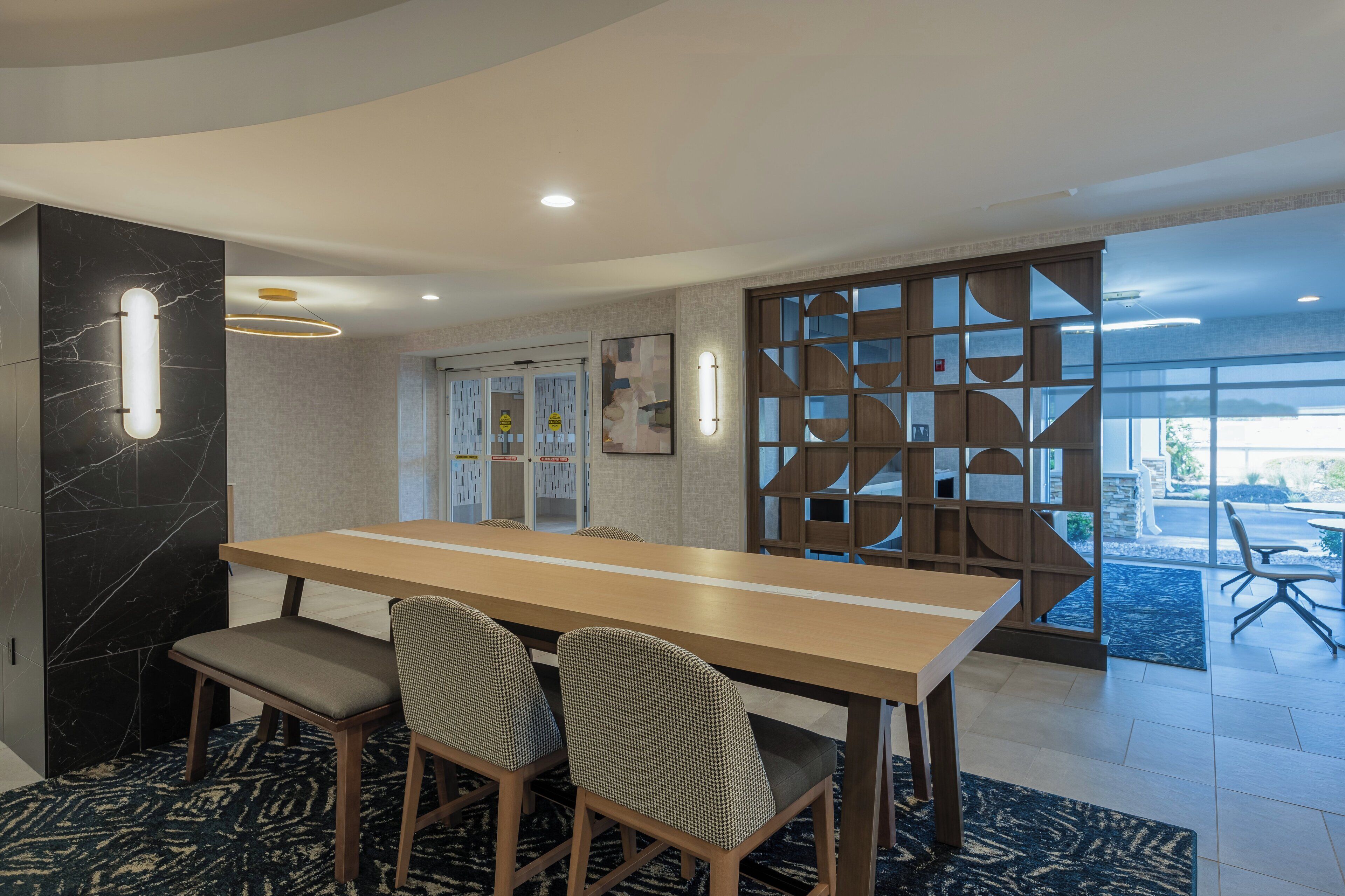 Uma sala de jantar moderna com uma mesa comprida e quatro cadeiras, uma parede de destaque em mármore e uma divisória decorativa de madeira.
