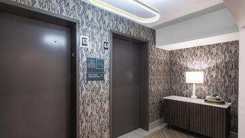Un moderno vestíbulo de hotel con dos ascensores, una recepción con una lámpara y un muro con diseño.