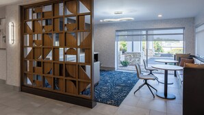 Une chambre d’hôtel moderne dotée d’une grande cloison coulissante en bois, d’un coin repas avec une table ronde et des chaises, et offrant une vue sur une terrasse extérieure grâce à de grandes fenêtres.