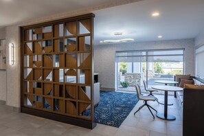A modern hotel room with a large sliding wooden partition, a dining area with a round table and chairs, and a view through large windows to an outdoor patio area. - Holiday Inn Anderson by IHG (Anderson)