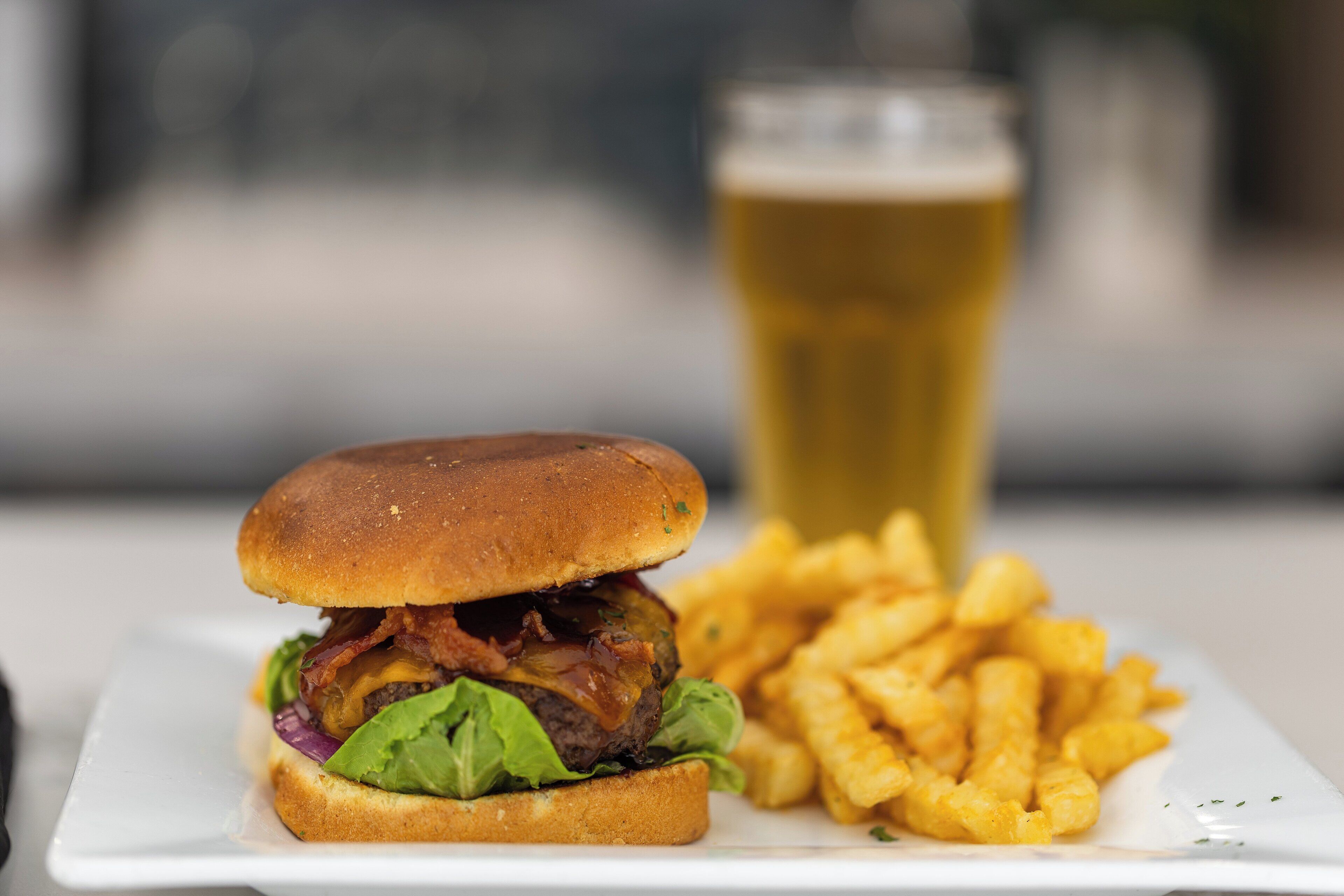 Ein Burger mit Pommes und einem Glas Bier auf einem weißen Teller.
