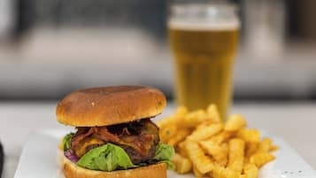 Una hamburguesa acompañada de papas fritas y una cerveza en un plato blanco.