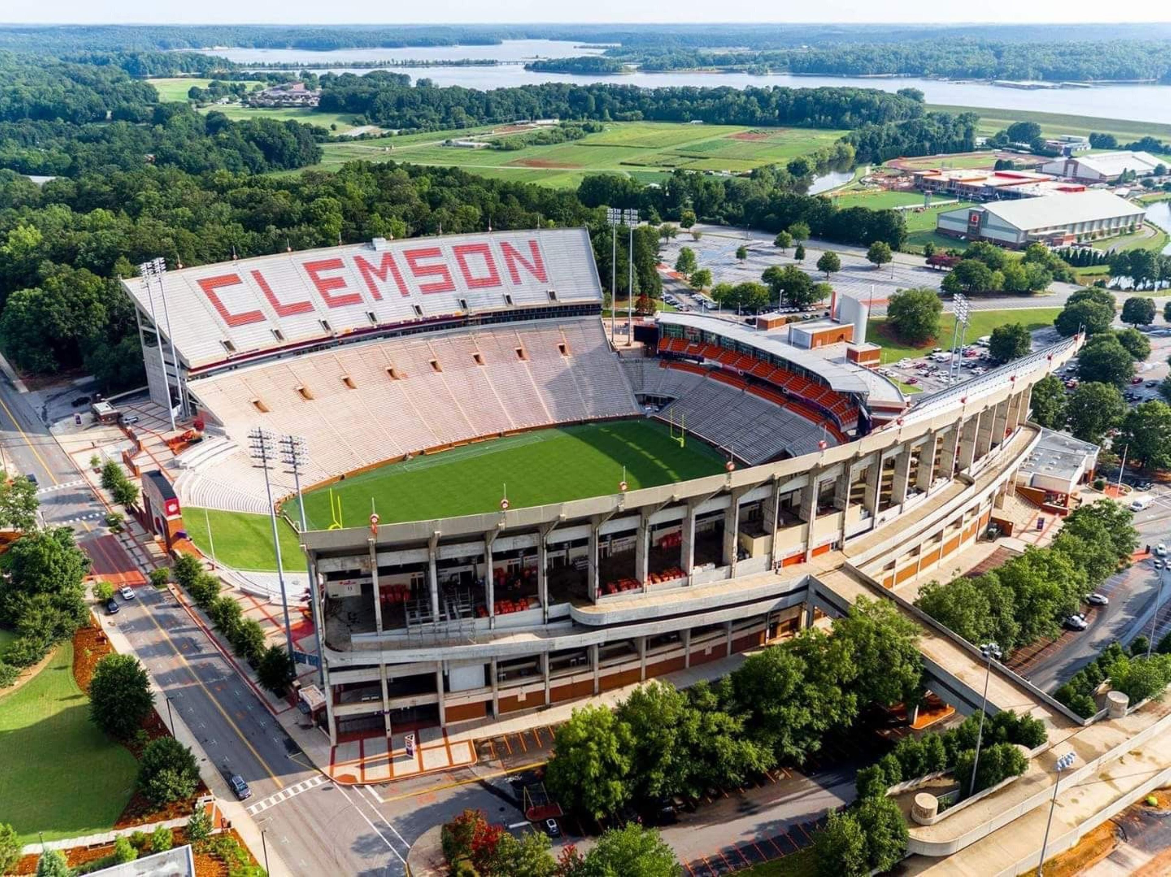 A stadium with 'CLEMSON' written on the upper deck, surrounded by greenery and a body of water.