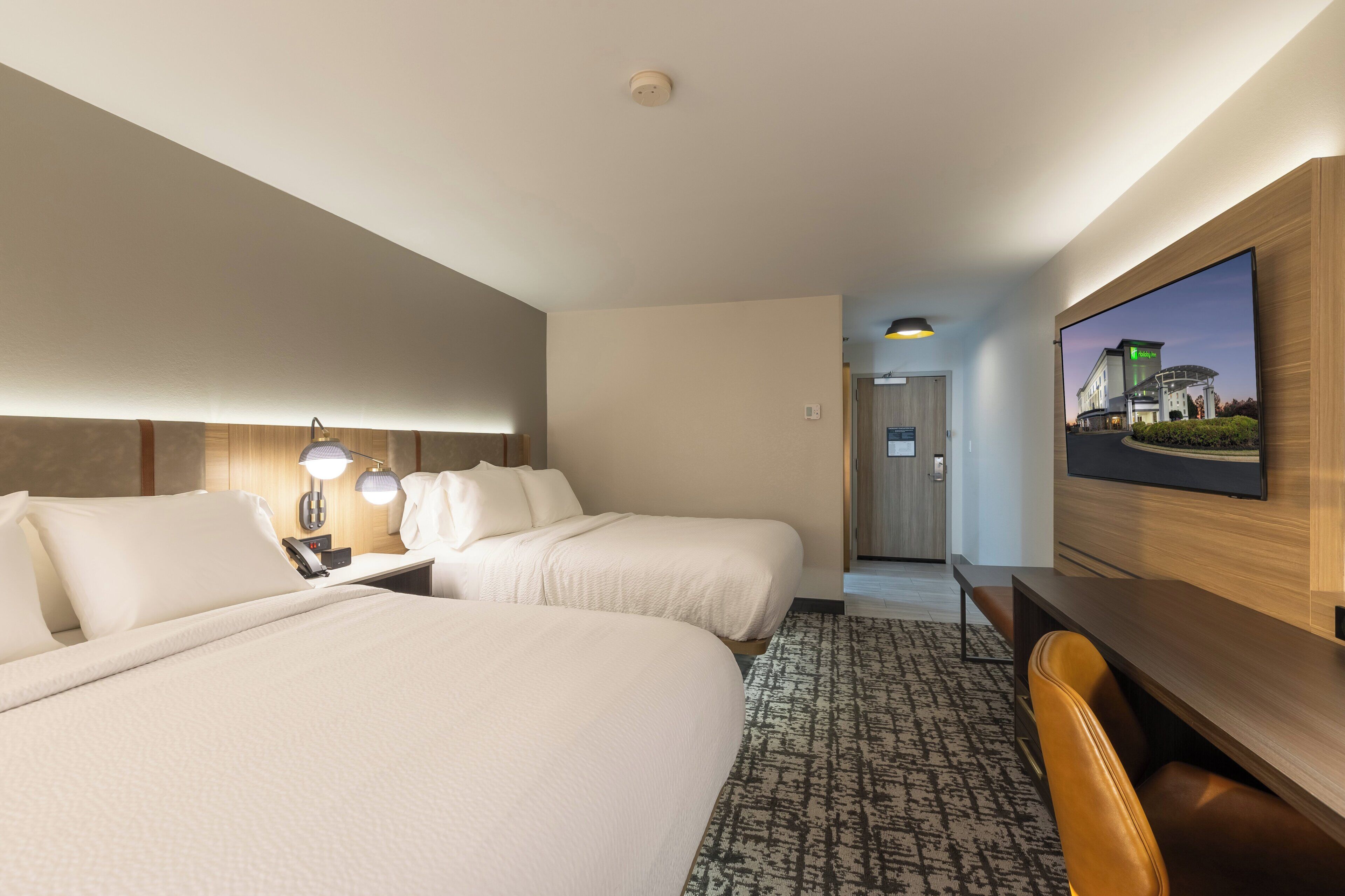 Une chambre d’hôtel avec deux lits, un bureau, une chaise, une télévision et une vue sur la façade de l’hôtel.